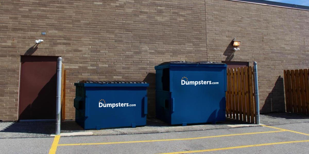 Two front load dumpsters in a commercial dumpster enclosure.