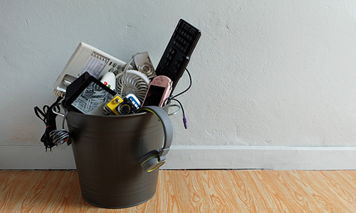 Electronic waste in a metal garbage can on a wood floor. 