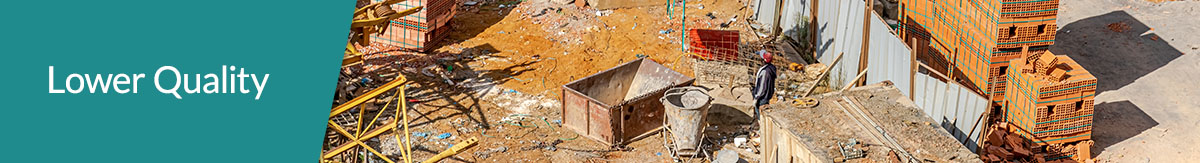 A yellow, crane-mounted truck on a messy jobsite with bricks and pallets lying about on reddish soil.