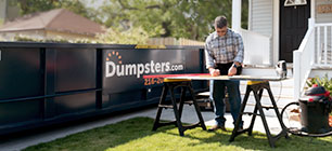 man working on sawhorses next to a rental dumpster