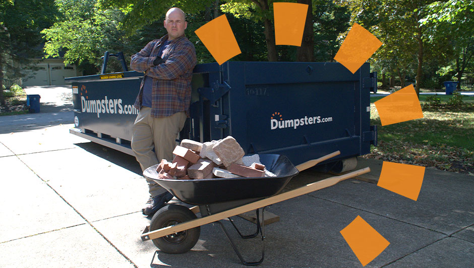 Man standing next to a dumpster and wheelbarrow filled with rocks