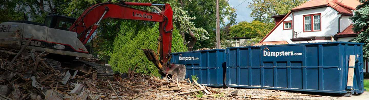 Two Blue 40 Yard Dumpsters With Dumpsters.com Logos Next to Construction Debris and Equipment