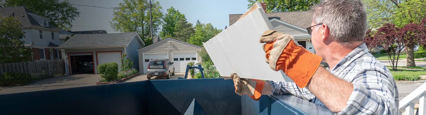 Man With Orange Work Gloves Tossing Wood Into a Dumpster