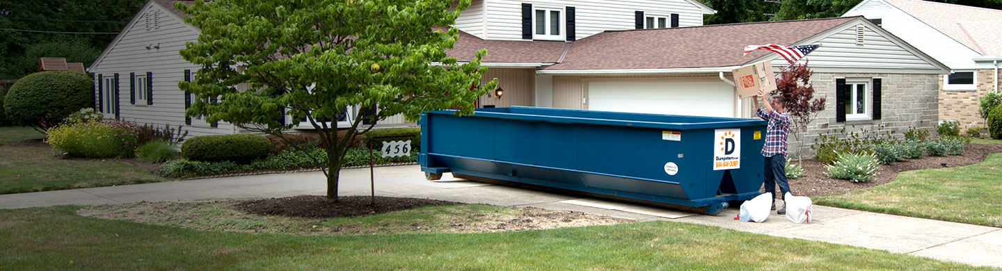 man loading a dumpster in a driveway