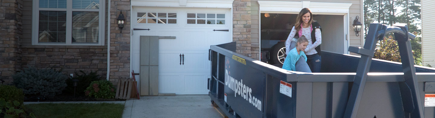 Mother and Daughter Loading Junk into Blue Residential Dumpster in Front of Nice House