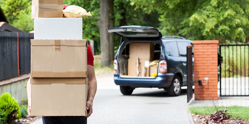 A Person Carries a Stack of Boxes to a Minivan.