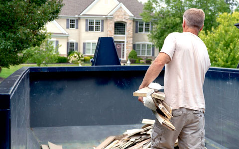 Man Loading Wood Planks Into a Temporary Dumpster