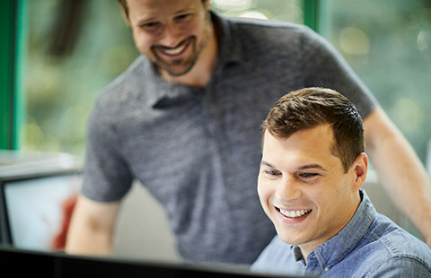 Two employees smile at a computer screen.