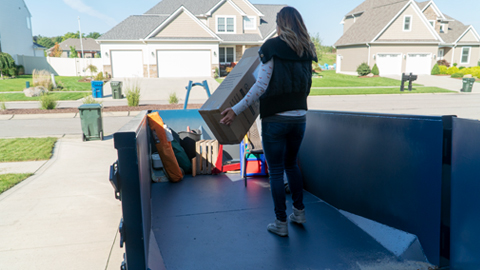 Woman Carrying Junk Into a Blue Roll Off Dumpster