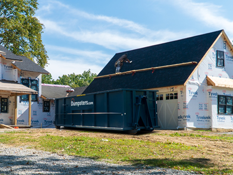 a roofer working on a new roof near a dumpsters.com roofing debris bin